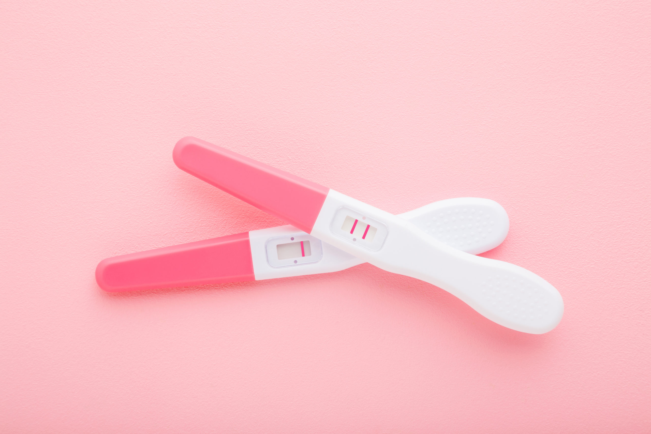 Pregnancy tests with one stripe and two stripes on light pink table background. Pastel color. Negative and positive result. Closeup. Top down view.